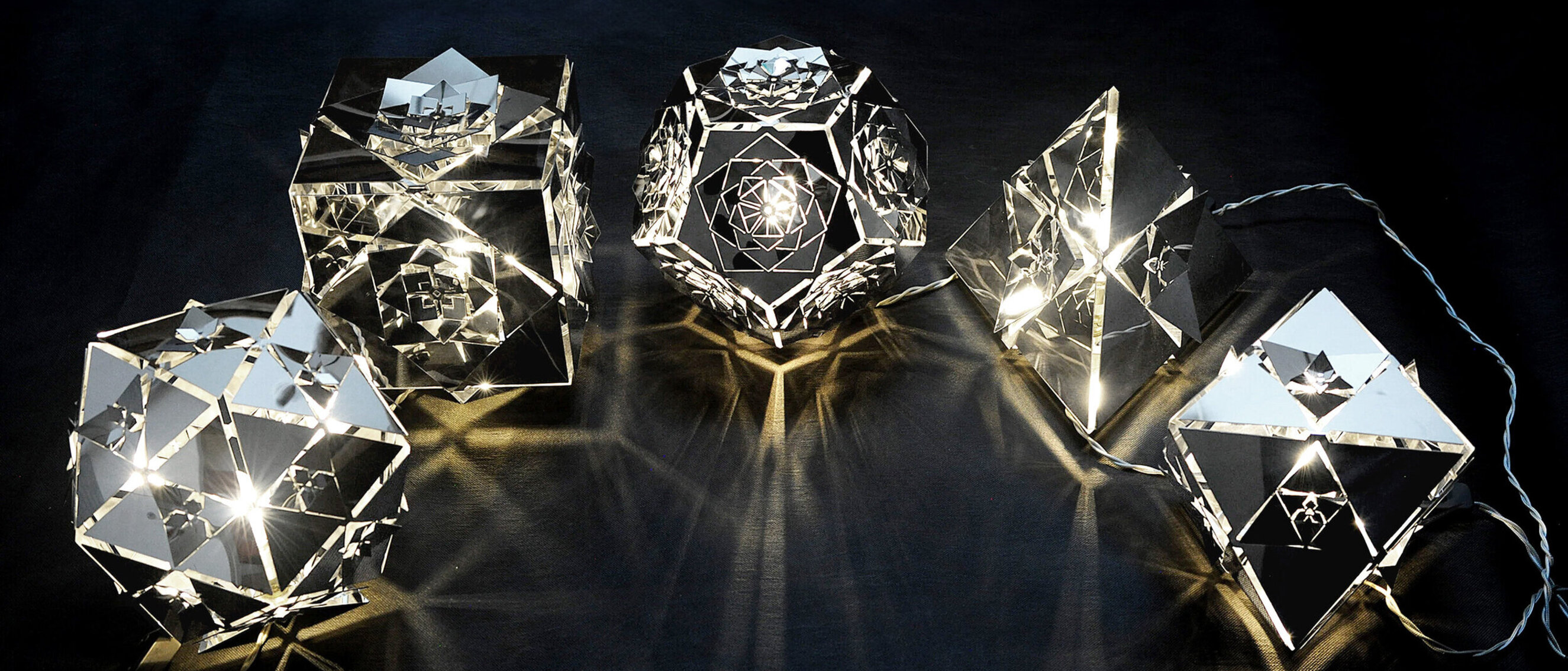 Platonic Solids Collection by KAGE: Set of Five Lamps A collection of five lamps by KAGE, each representing a different platonic solid, glowing warmly against a dark backdrop.