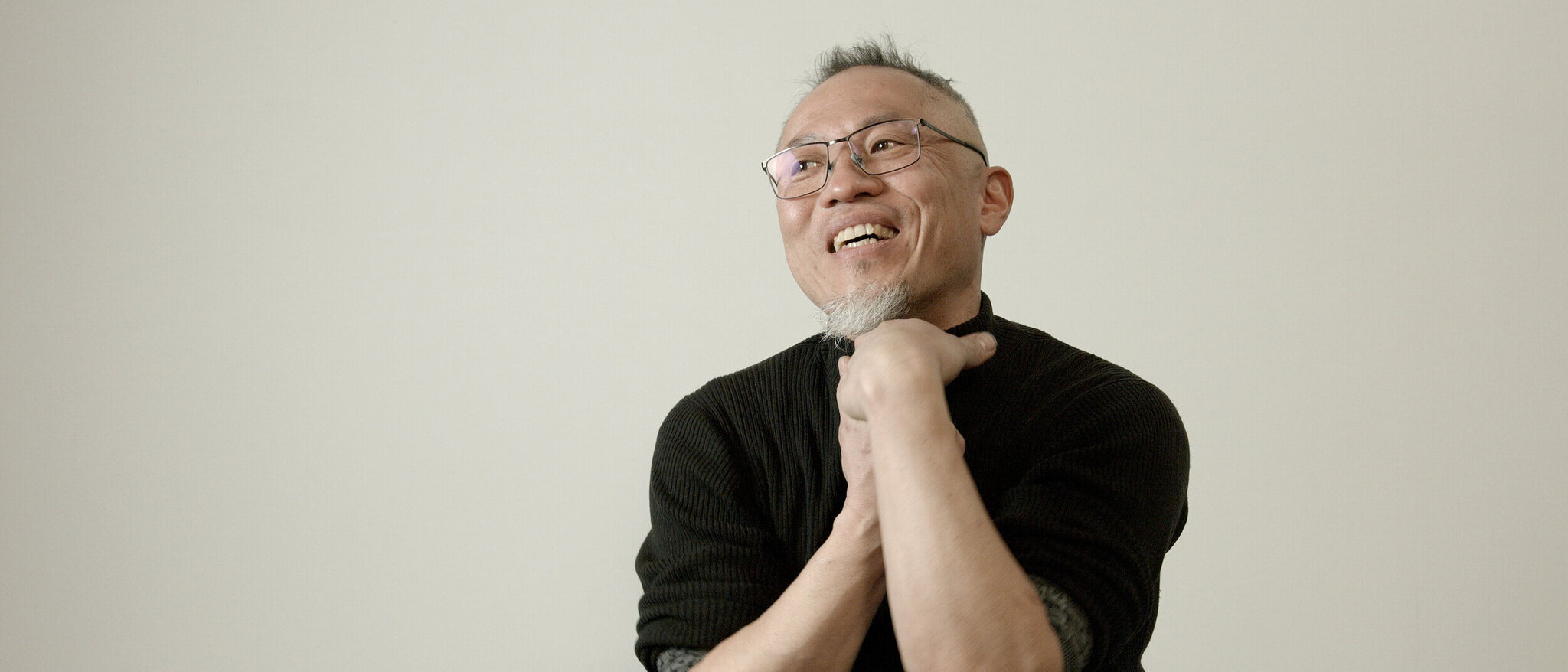 Portrait of Daniel KAGE Daniel KAGE, in glasses and a black sweater, thoughtfully looking up and to the side with his hand on his chin.